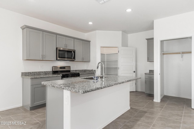 kitchen featuring stainless steel appliances, light stone countertops, a sink, and gray cabinets