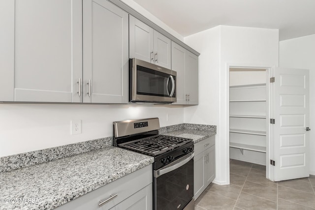 kitchen with light tile patterned flooring, gray cabinetry, light stone countertops, and stainless steel appliances