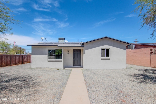 view of front of property featuring a fenced backyard, solar panels, and stucco siding
