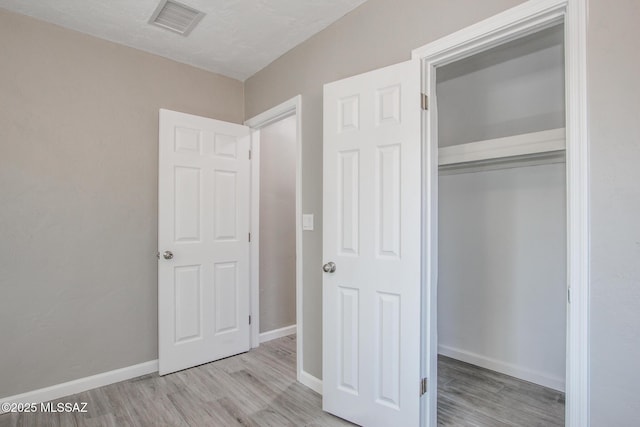 unfurnished bedroom with a closet, visible vents, baseboards, and wood finished floors