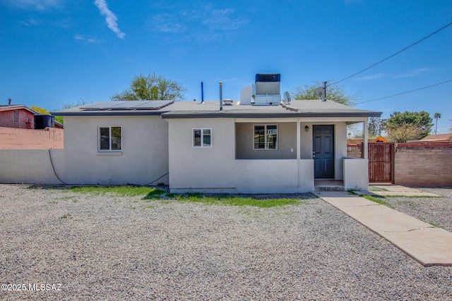 back of house featuring central AC, stucco siding, fence, solar panels, and a gate