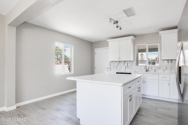 kitchen featuring white cabinets, visible vents, a kitchen island, light countertops, and decorative backsplash