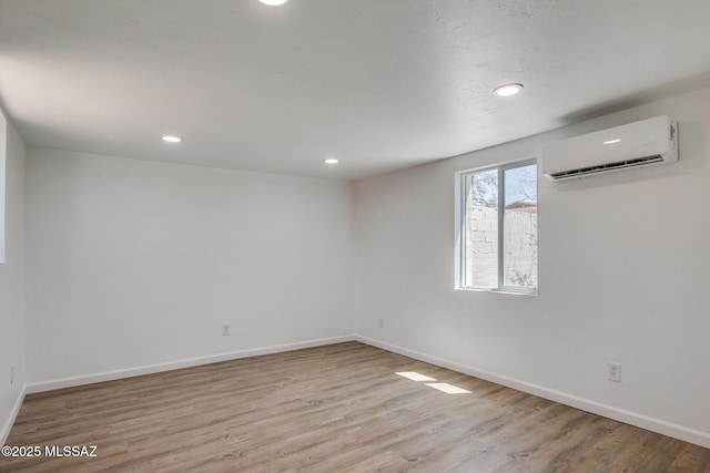 unfurnished room featuring a wall mounted AC, wood finished floors, baseboards, and recessed lighting