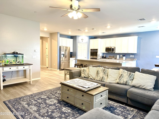 living area with visible vents, light wood-style flooring, ceiling fan, and baseboards
