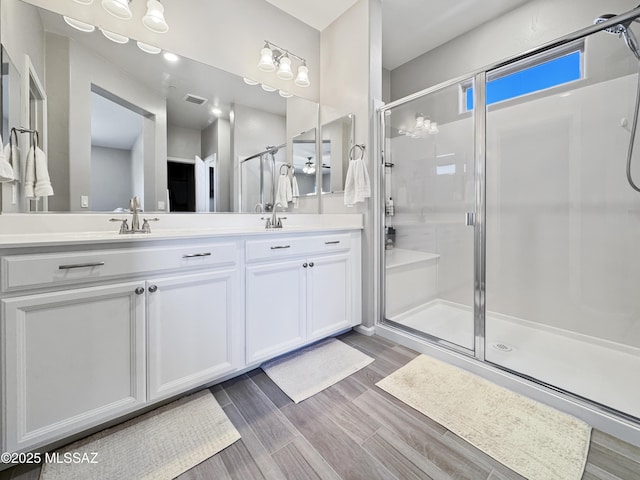 full bath featuring double vanity, visible vents, a shower stall, and wood finished floors