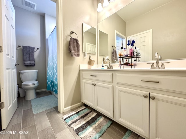 bathroom with visible vents, double vanity, wood finished floors, toilet, and a sink