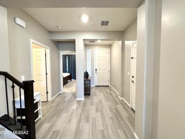 corridor featuring visible vents, baseboards, stairs, and light wood-type flooring