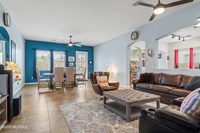 tiled living room featuring a ceiling fan, baseboards, arched walkways, and rail lighting