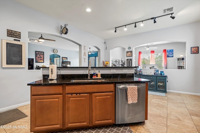 kitchen featuring dark stone countertops, stainless steel dishwasher, a sink, arched walkways, and ceiling fan