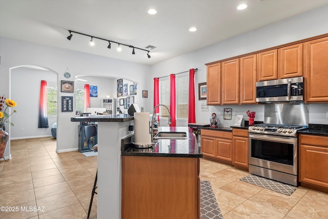 kitchen featuring arched walkways, a sink, a kitchen bar, an island with sink, and appliances with stainless steel finishes