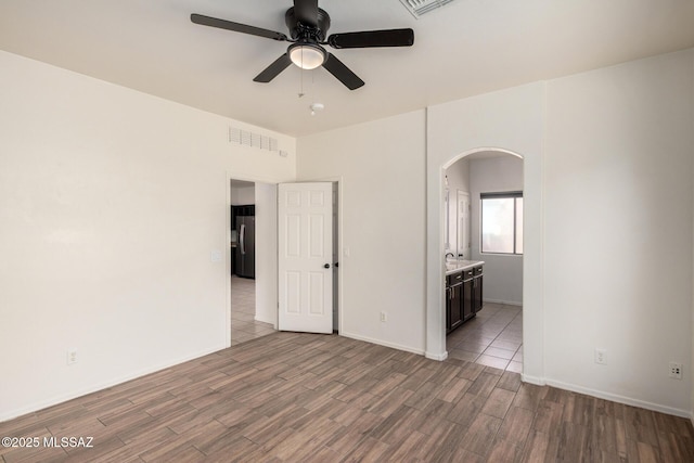 unfurnished bedroom with visible vents, arched walkways, wood finished floors, baseboards, and freestanding refrigerator
