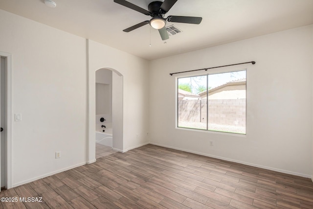 empty room with visible vents, wood finished floors, baseboards, ceiling fan, and arched walkways