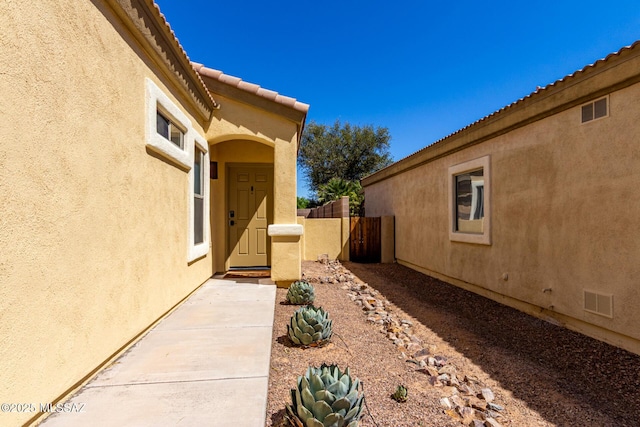 property entrance featuring fence, stucco siding, and visible vents