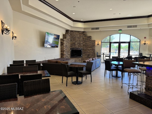 living area with light tile patterned floors, crown molding, a stone fireplace, and visible vents