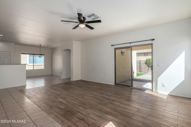 unfurnished living room with wood finish floors, arched walkways, ceiling fan with notable chandelier, baseboards, and visible vents