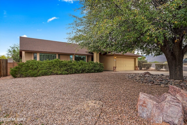 view of front of house with an attached garage, driveway, stucco siding, and fence