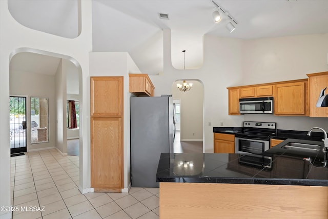 kitchen featuring rail lighting, arched walkways, high vaulted ceiling, and stainless steel appliances