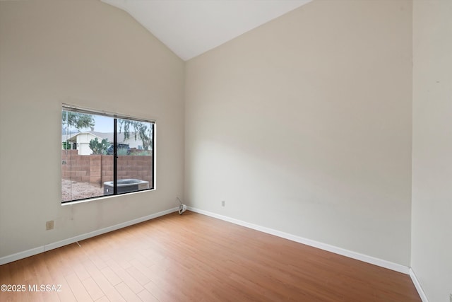 empty room featuring baseboards, high vaulted ceiling, and wood finished floors