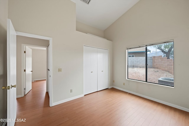 unfurnished bedroom with high vaulted ceiling, baseboards, a closet, and wood finished floors