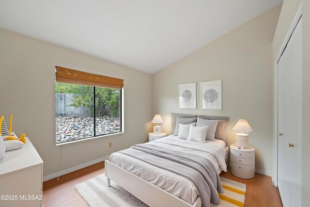 bedroom with baseboards, lofted ceiling, light wood finished floors, and a closet