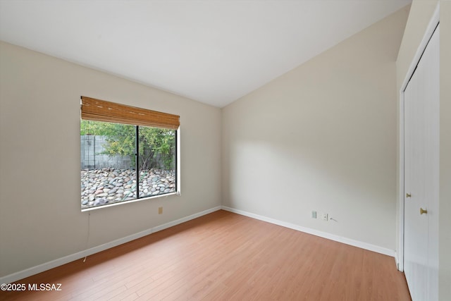 empty room with baseboards, vaulted ceiling, and light wood-style flooring