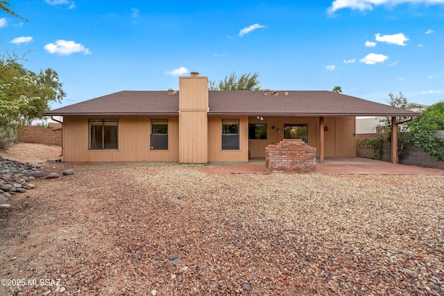 back of property featuring fence, a chimney, a patio area, and roof with shingles