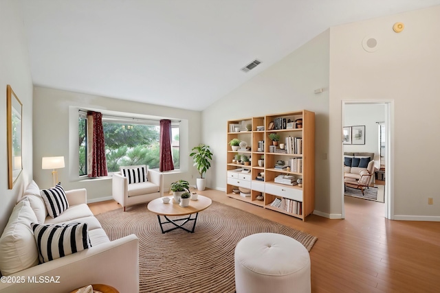 living area with high vaulted ceiling, baseboards, wood finished floors, and visible vents