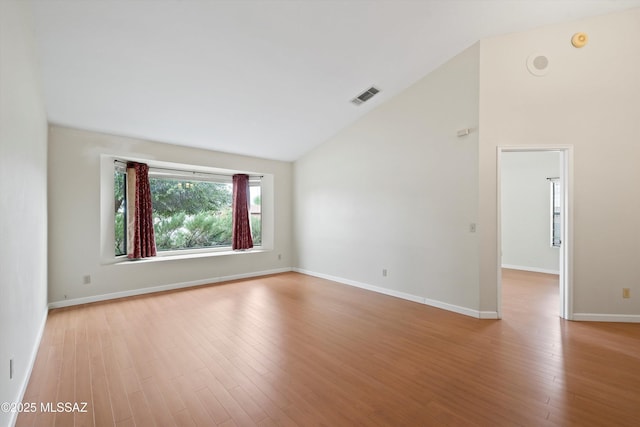 empty room with high vaulted ceiling, visible vents, baseboards, and light wood-type flooring