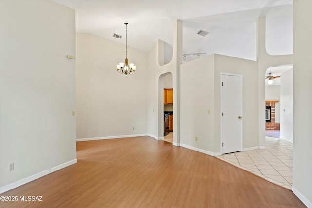 interior space featuring arched walkways, high vaulted ceiling, light wood-style flooring, baseboards, and visible vents
