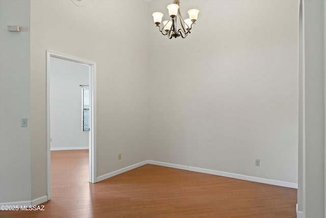 spare room featuring baseboards, wood finished floors, and a notable chandelier