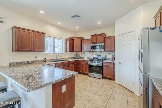 kitchen with light tile patterned floors, a kitchen bar, a peninsula, appliances with stainless steel finishes, and a sink