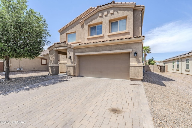 mediterranean / spanish house with stucco siding, a tiled roof, decorative driveway, and an attached garage