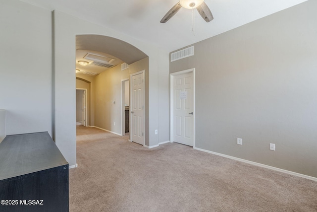 spare room with visible vents, baseboards, arched walkways, ceiling fan, and light carpet