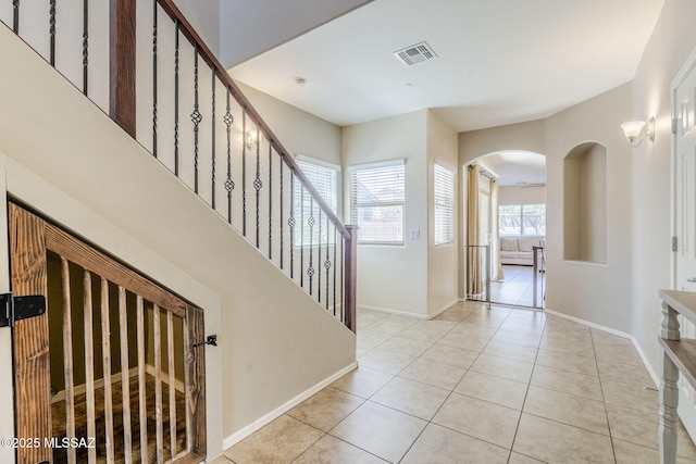 foyer featuring visible vents, baseboards, light tile patterned floors, arched walkways, and stairs