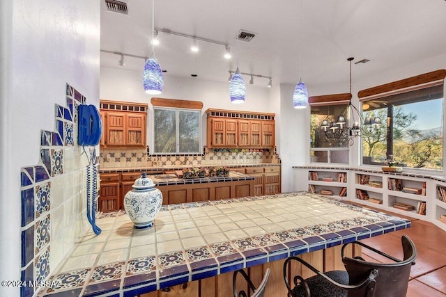 interior space with brown cabinetry, track lighting, tile patterned flooring, decorative backsplash, and tile counters