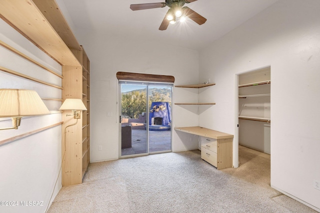 unfurnished office featuring built in desk, ceiling fan, and light colored carpet