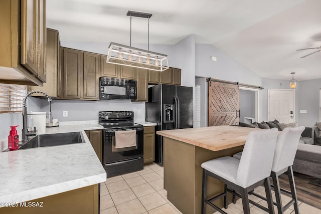 kitchen featuring a barn door, lofted ceiling, a sink, black appliances, and a kitchen bar