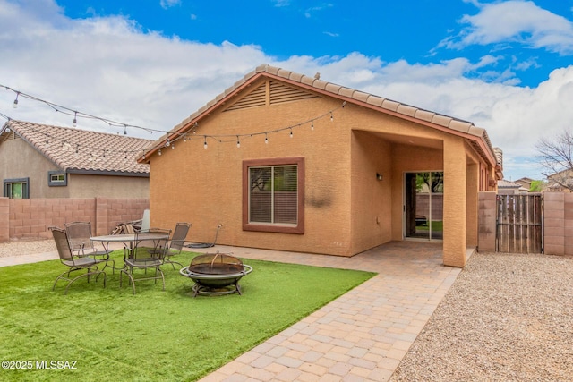 back of property with stucco siding, a yard, a fenced backyard, and an outdoor fire pit