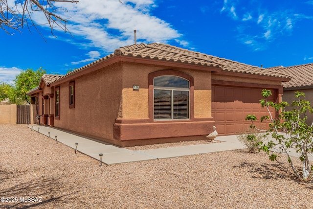 view of side of home with stucco siding, a tiled roof, and a garage