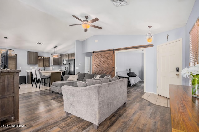 living area featuring a barn door, ceiling fan, wood finished floors, and visible vents