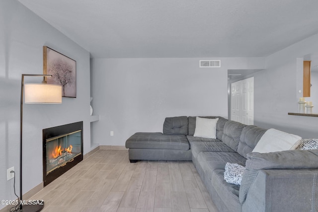 101 S Players Club Dr Unit 12103, Tucson, AZ 85745 - living room with a glass covered fireplace, visible vents, baseboards, and light wood-style flooring