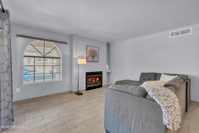 101 S Players Club Dr Unit 12103, Tucson, AZ 85745 - living area with a textured ceiling, a glass covered fireplace, visible vents, wood tiled floor, and baseboards