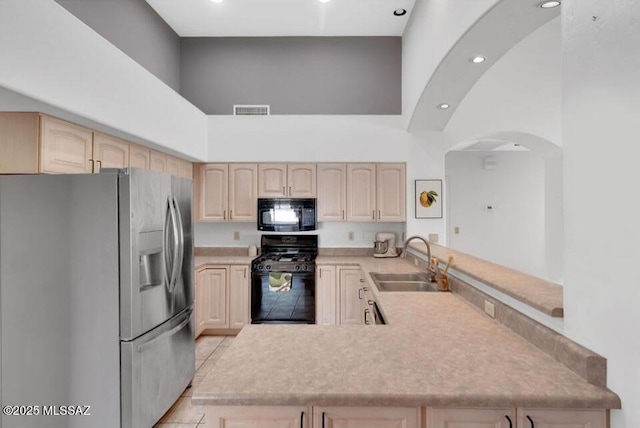 kitchen with black appliances, a towering ceiling, light brown cabinetry, and a sink