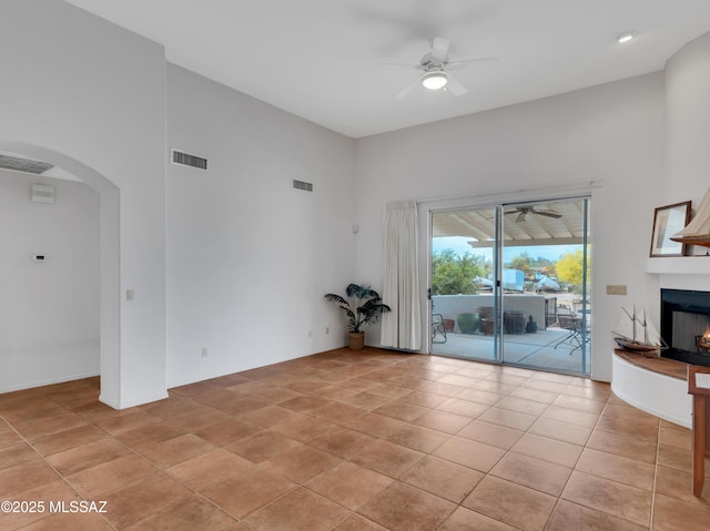 unfurnished living room with ceiling fan, arched walkways, a high ceiling, and visible vents