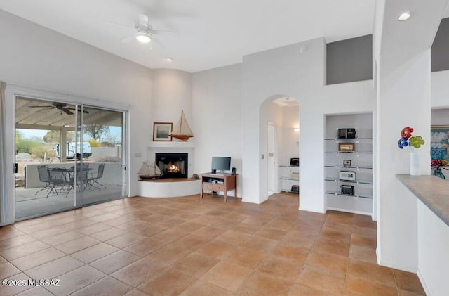 living area with a lit fireplace, a towering ceiling, arched walkways, and ceiling fan