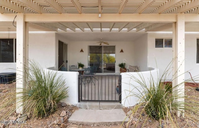 entrance to property with ceiling fan, a pergola, and stucco siding