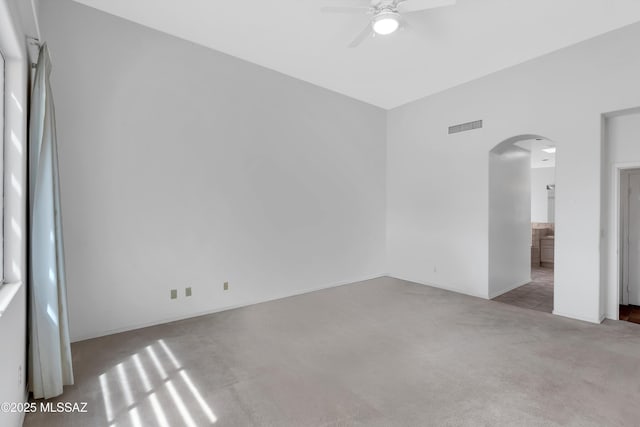 empty room with carpet, visible vents, arched walkways, baseboards, and ceiling fan