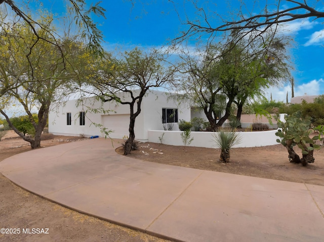 view of front facade with a garage, driveway, stucco siding, and fence