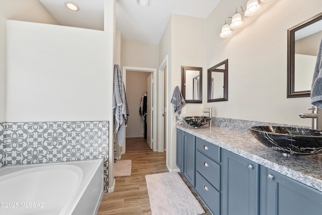 bathroom featuring a bath, wood finished floors, a sink, and double vanity