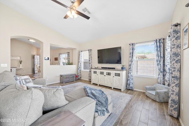 living room with vaulted ceiling, ceiling fan, arched walkways, baseboards, and visible vents